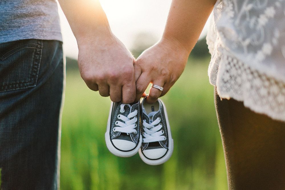 A couple holding hands, with a pair of baby shoes